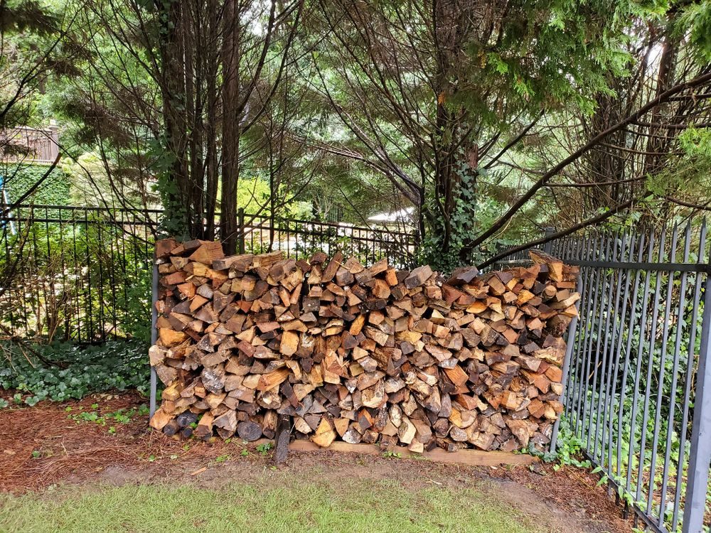 Split firewood stacked against iron fence — Major Firewood Delivery